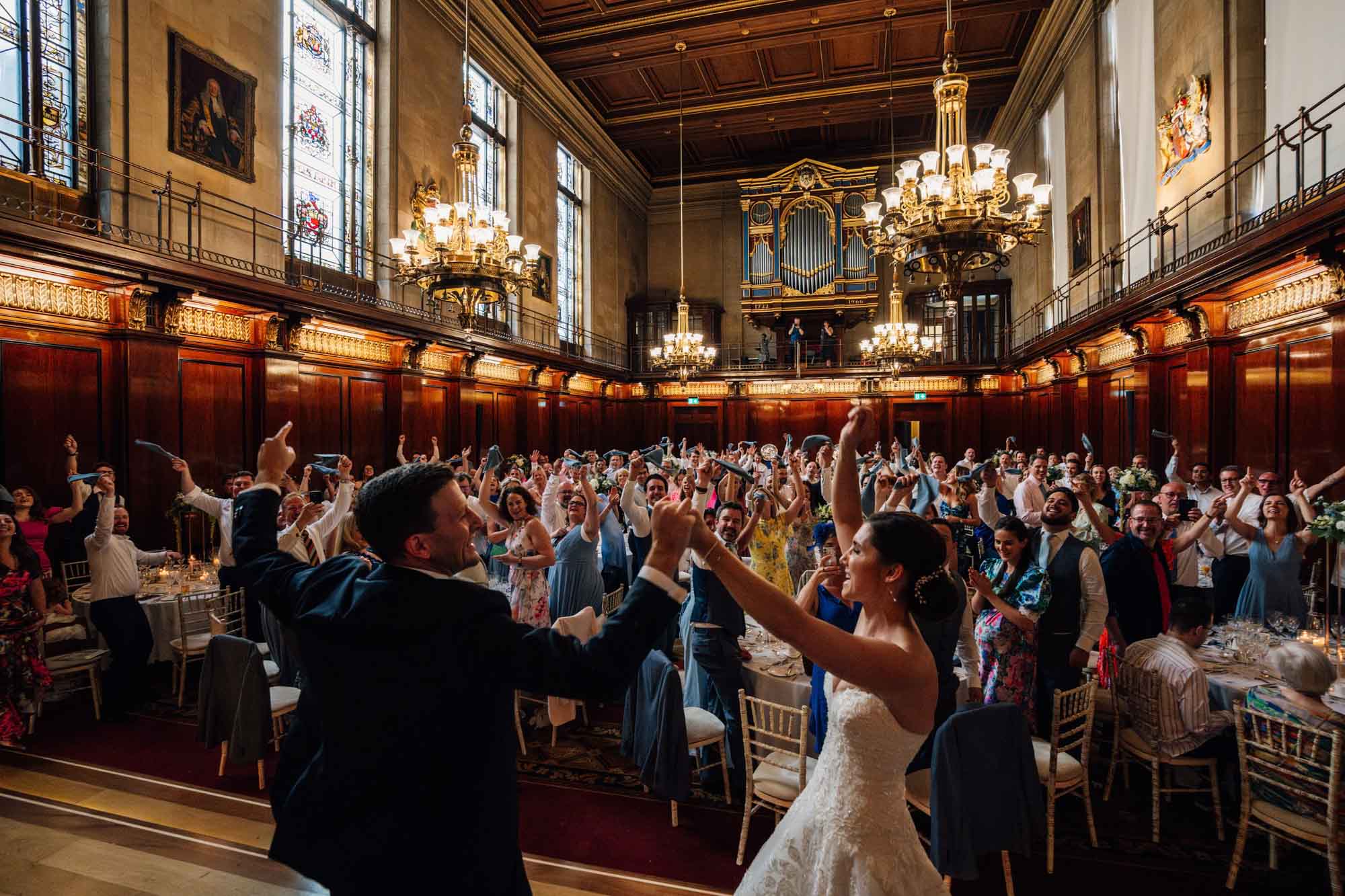 bride and groom celebrating in front of their guests in the great hall at their Merchant Taylors' Hall wedding