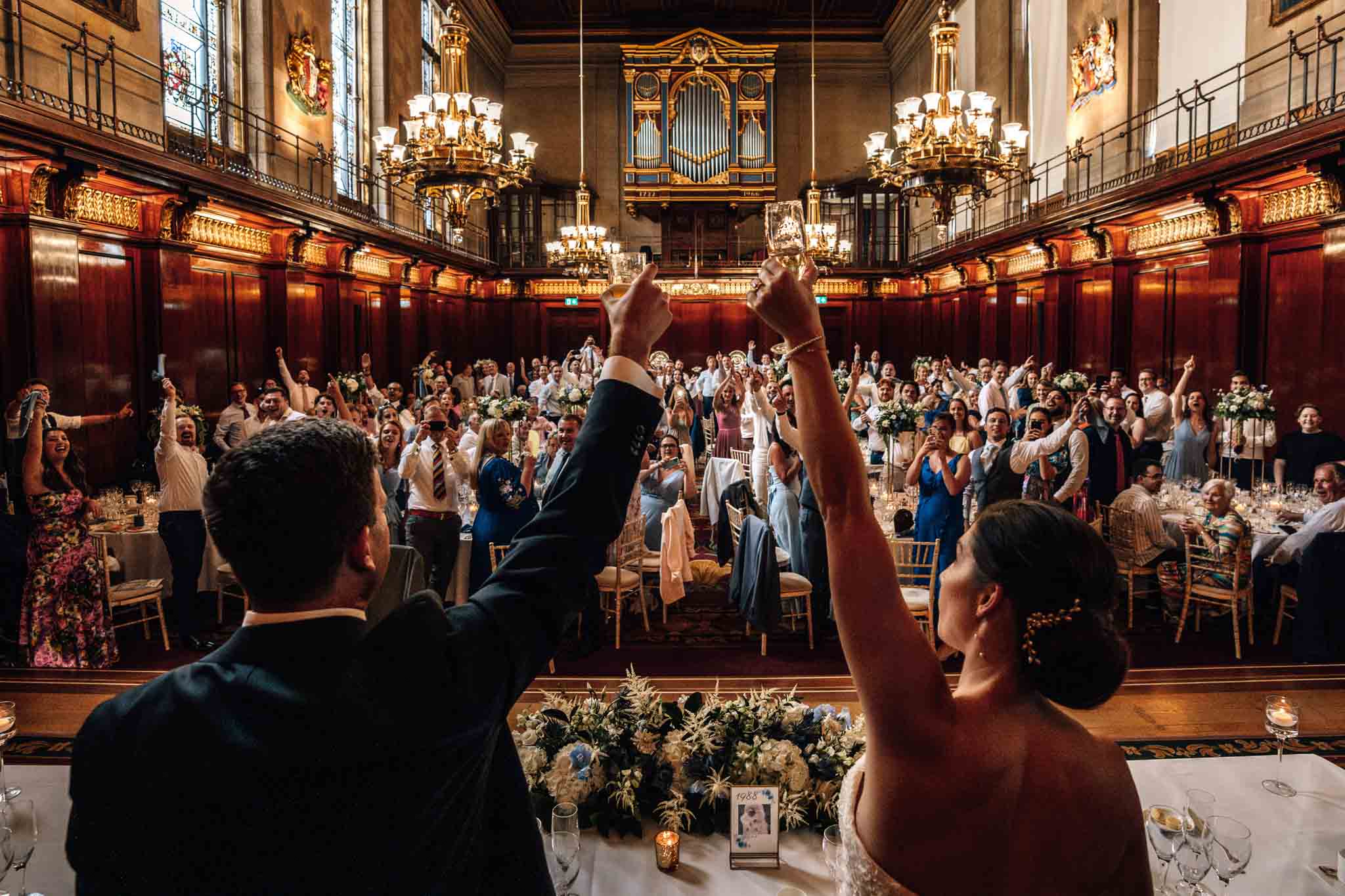 Bride and groom raise a toast in the Great Hall, captured in Merchant Taylors' Hall wedding photography, by Ben Lee