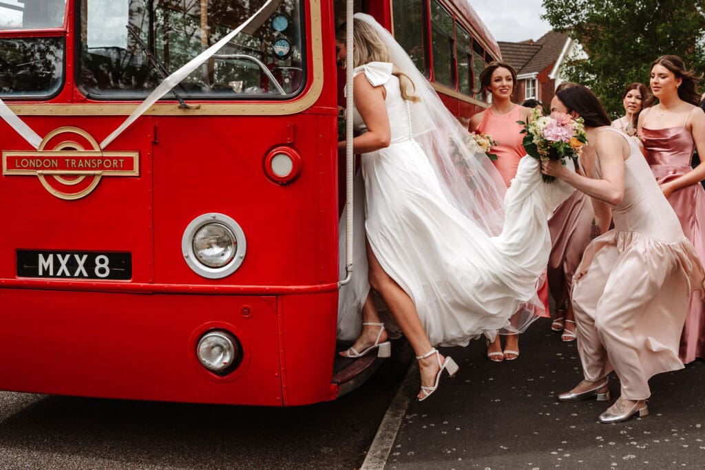 bride getting onto red bus by Eastfield Barn wedding photographer, Ben Lee.
