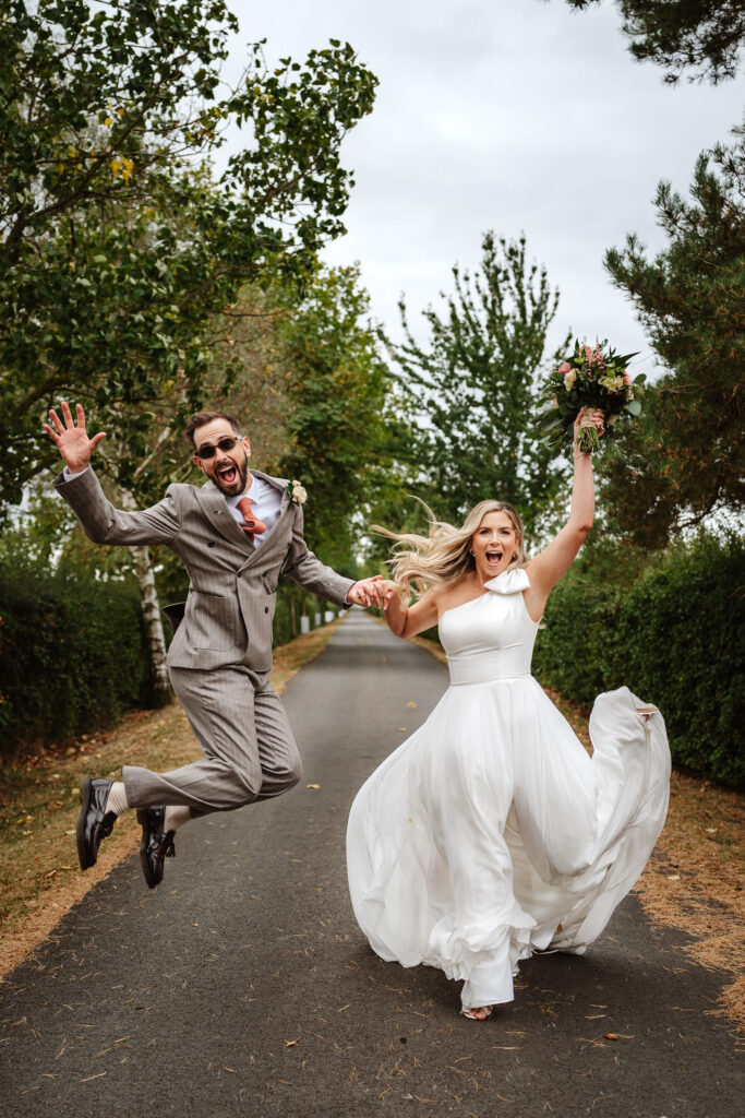 bride and groom jumping for joy by Eastfield Barn wedding photographer, Ben Lee.