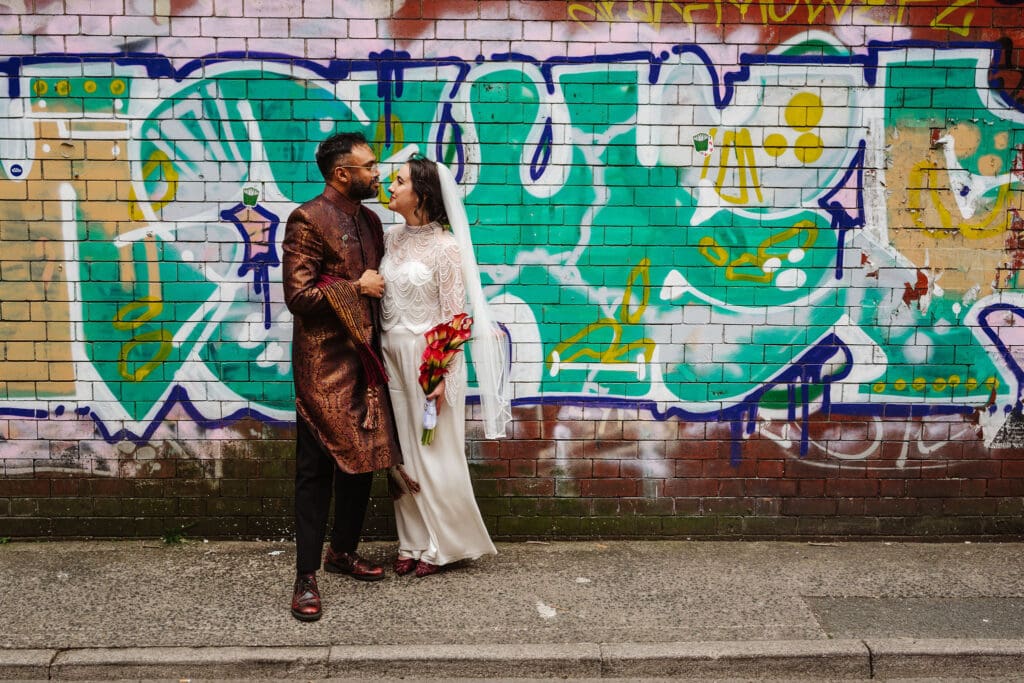 bride and groom in front of street art on a wall in Manchester on their walk to their cinema wedding in Manchester, captured by Ben Lee Photography 