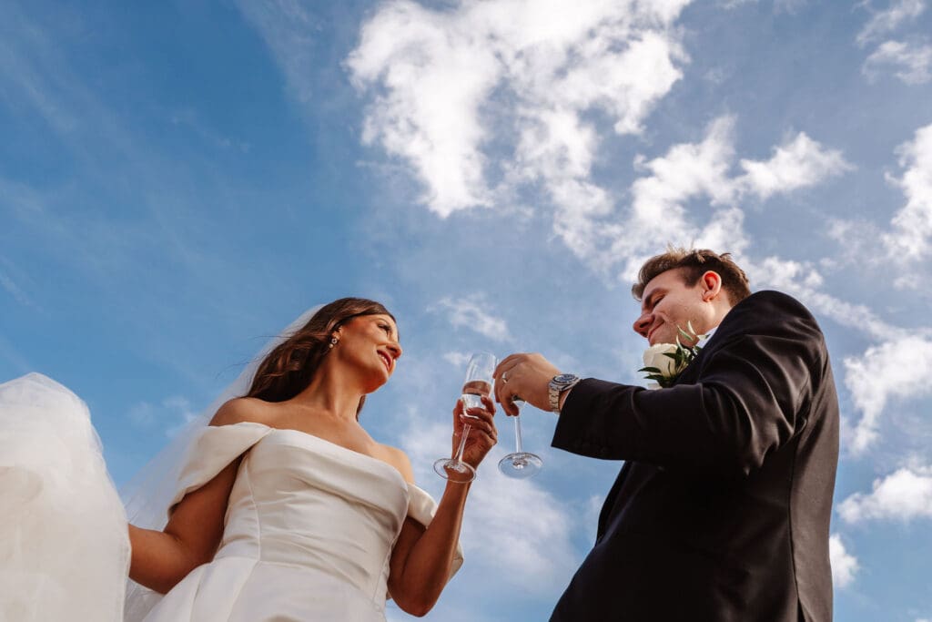 Bride and groom with champagne under blue sky captured by Ben Lee Photography